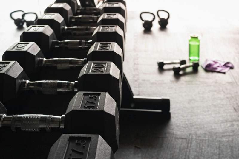 A row of black hex dumbbells on a rack in a bright gym
